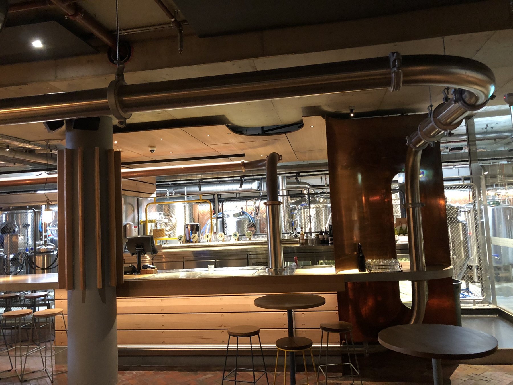 Copper beer python over a brewpub bar with brewing tanks behind